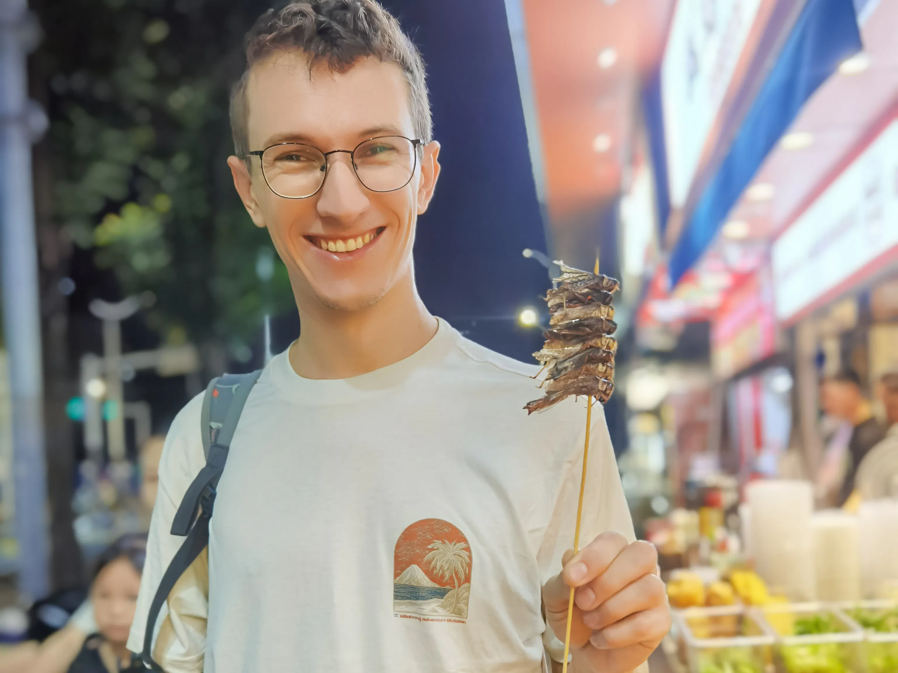 Man enjoying street food skewer in Shenzhen night market.