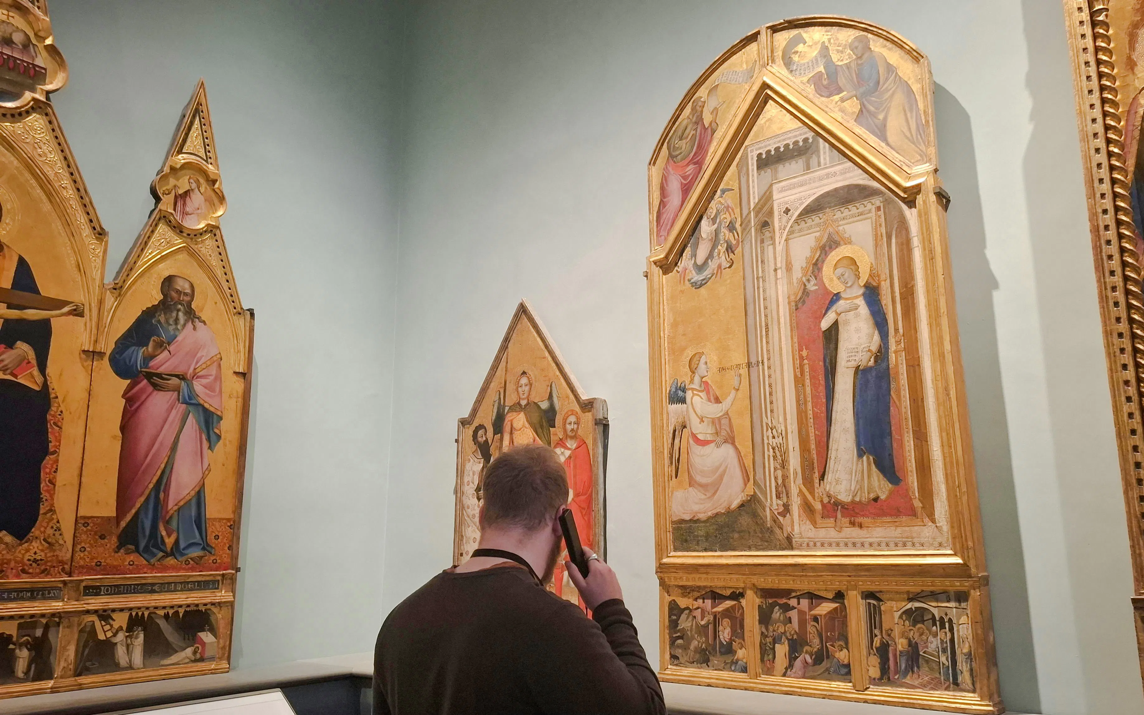 Visitor using audio guide at Academia Gallery, viewing religious paintings, Florence.