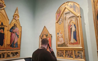 Visitor using audio guide at Academia Gallery, viewing religious paintings, Florence.