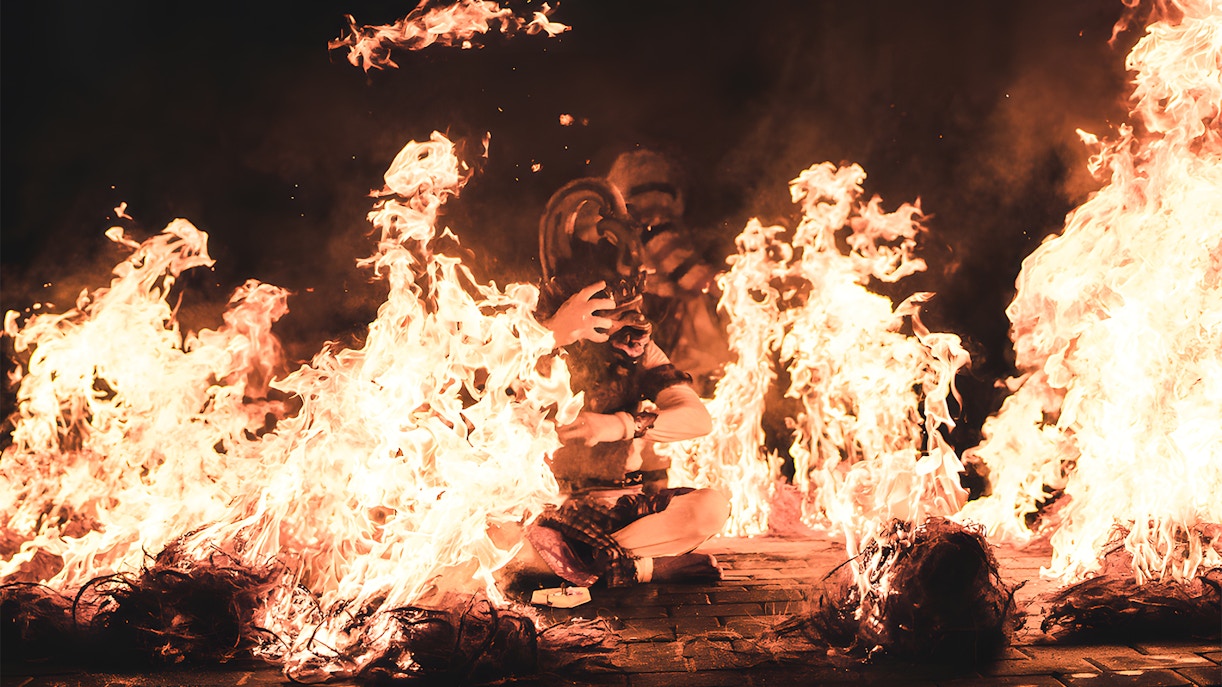 Kecak dancer surrounded by fire during a performance by the beach.