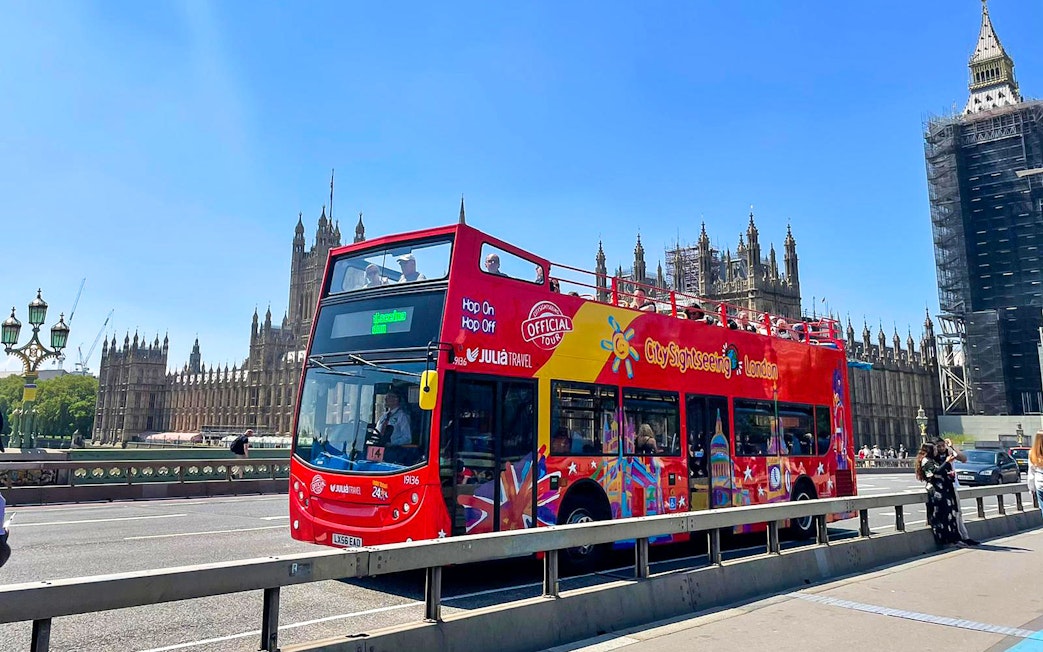 Open-top red tour bus on Westminster Bridge with Houses of Parliament in London.