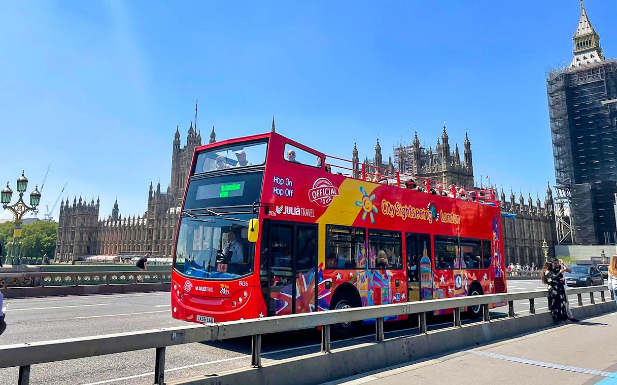Open-top red tour bus on Westminster Bridge with Houses of Parliament in London.