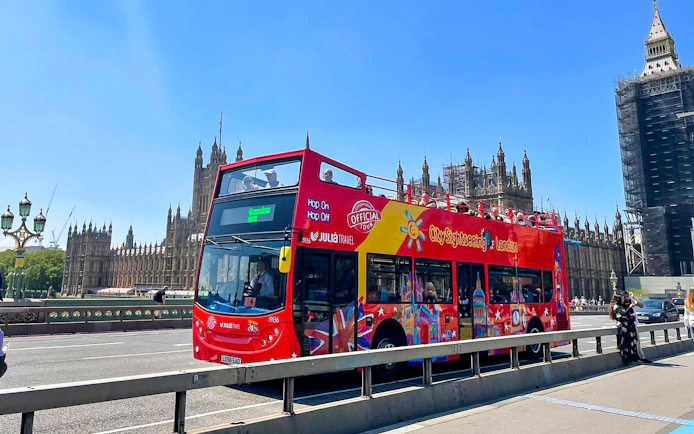 Open-top red tour bus on Westminster Bridge with Houses of Parliament in London.