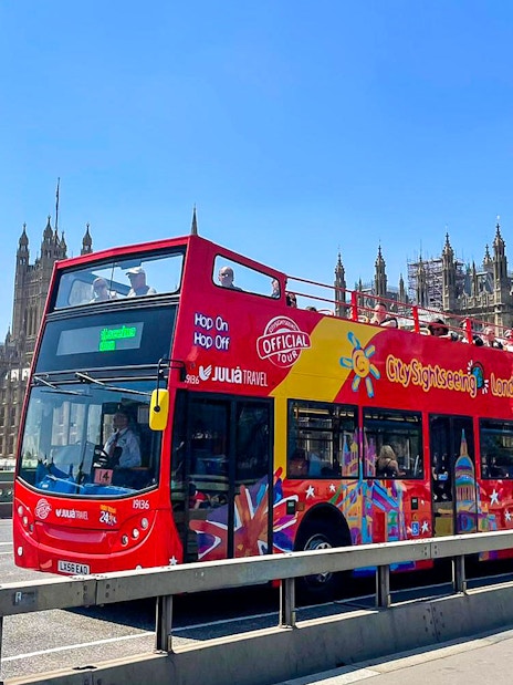 Open-top red tour bus on Westminster Bridge with Houses of Parliament in London.