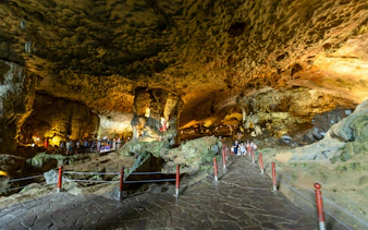 Hang Sung Sot Cave interior with tourists exploring limestone formations in Ha Long Bay, Vietnam.