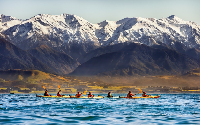 Kayakers paddling on a lake with snow-capped mountains in the background.
