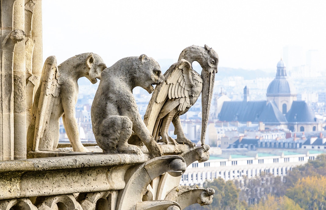 Chimeras on Notre-Dame de Paris tower gallery overlooking Paris cityscape.