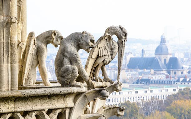 Three stone chimeras on Notre-Dame de Paris tower gallery overlooking the city.