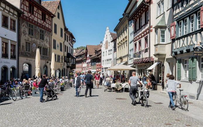 Pedestrian zone in Stein am Rhein old town with people dining and walking along historic buildings.