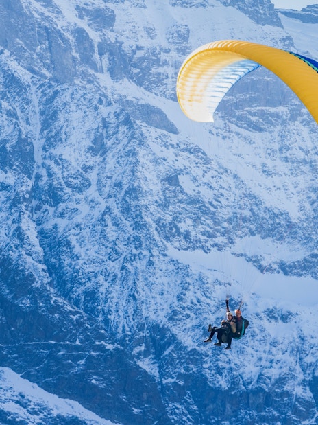 Paragliders soaring over snowy mountains in Interlaken.