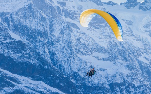 Paragliders soaring over snowy mountains in Interlaken.