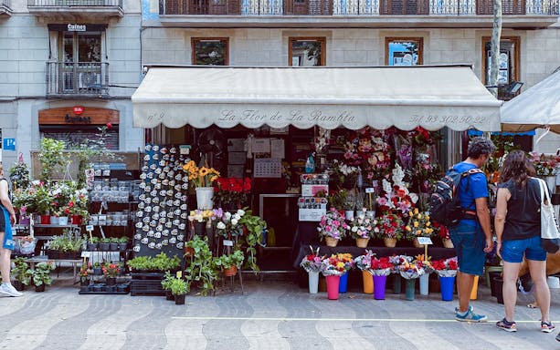 Flower shop on La Rambla, Barcelona, with tourists browsing colorful bouquets and plants.