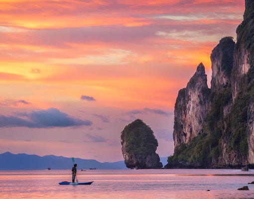 Kayaker at sunset near limestone cliffs, Phi Phi Islands, Thailand.