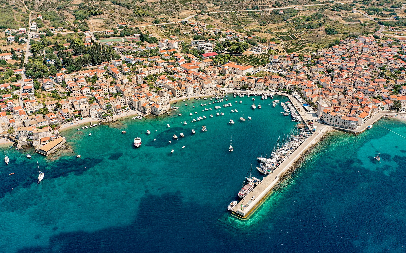 Aerial view of Komiza, Croatia with boats in the harbor and red-roofed buildings.