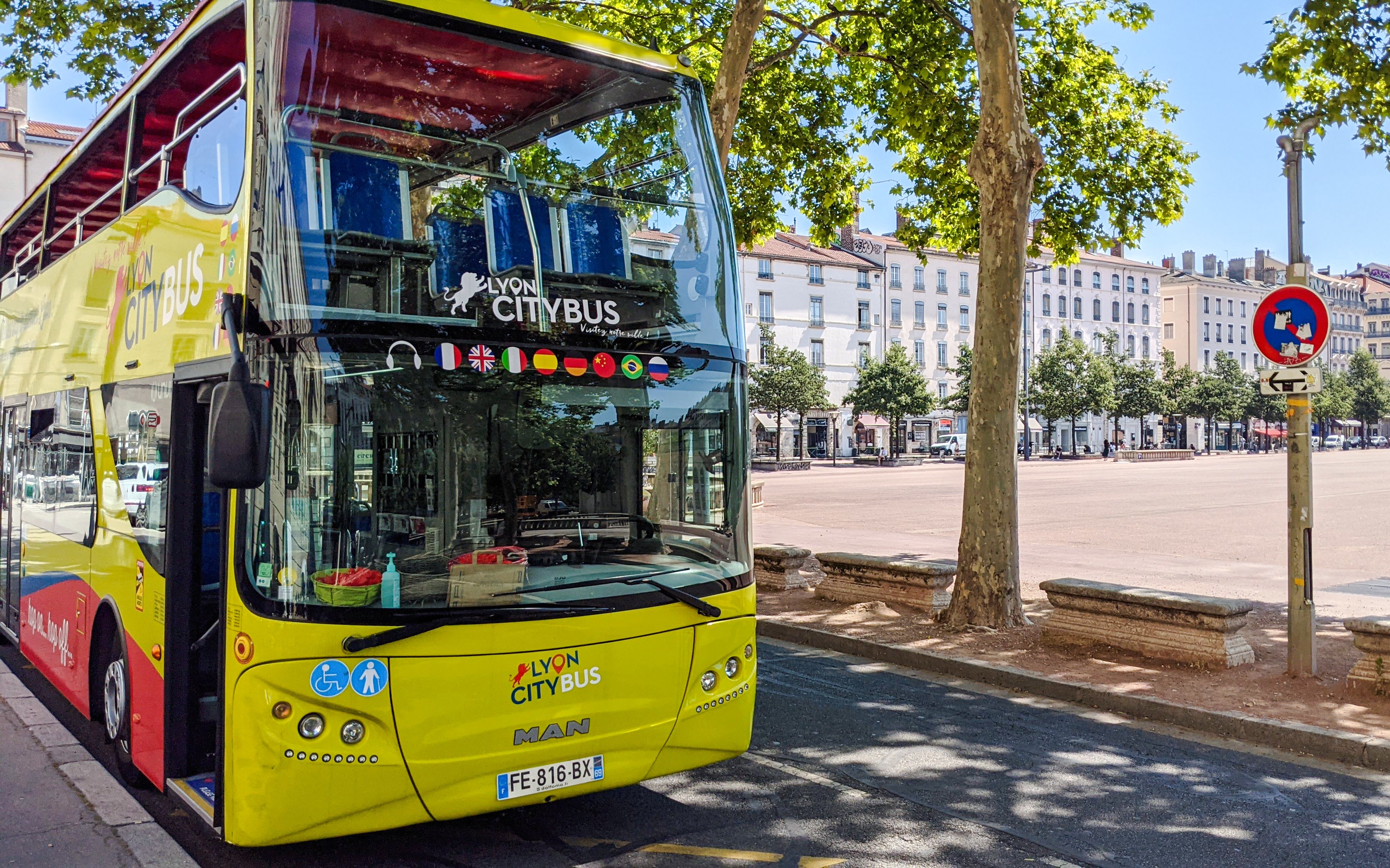 Lyon city tour bus parked near a tree-lined square in France.