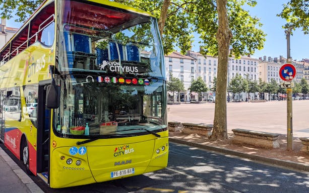 Lyon city tour bus parked near a tree-lined square in France.