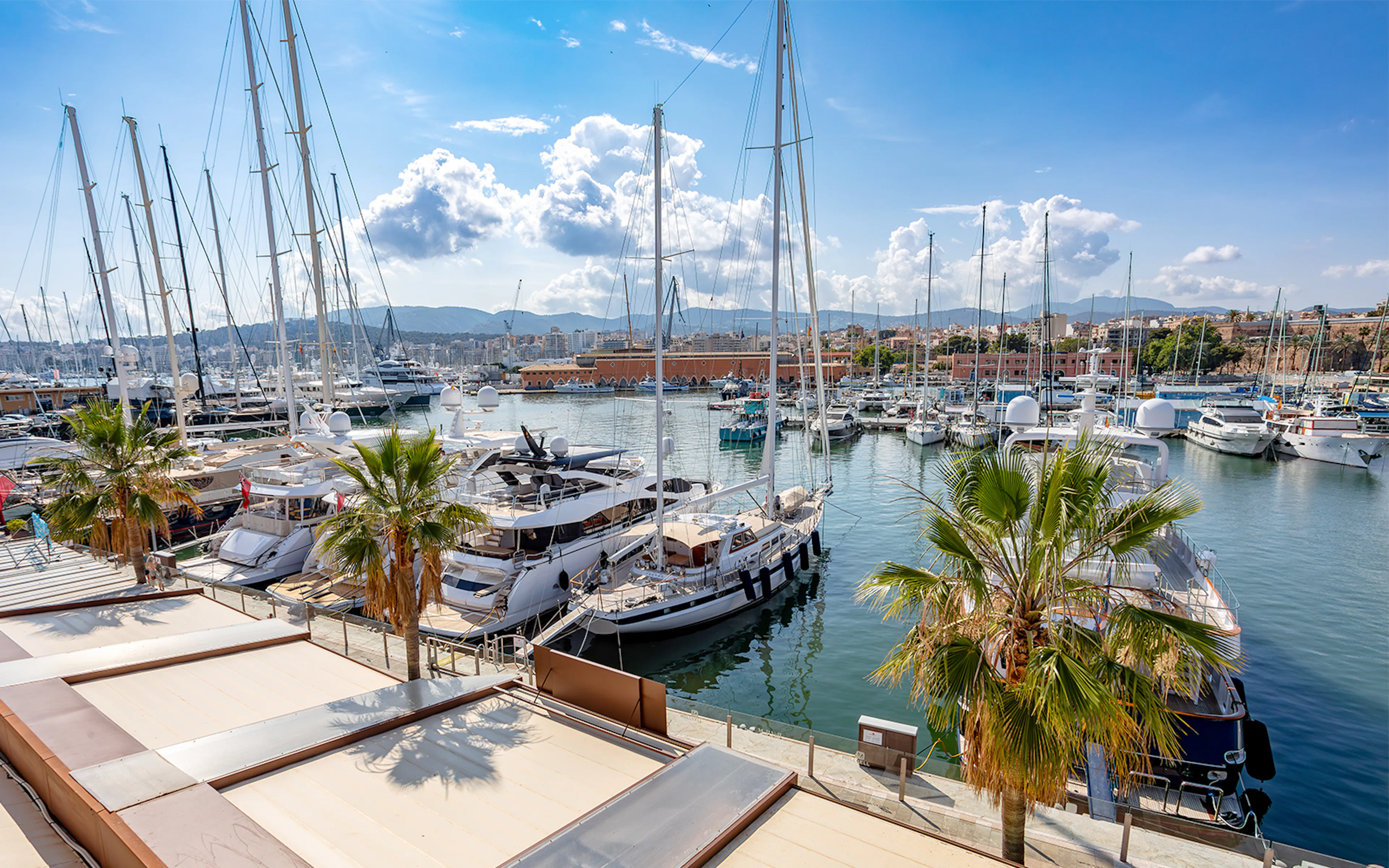Boats docked at Palma Port in Mallorca with cityscape and mountains in the background.