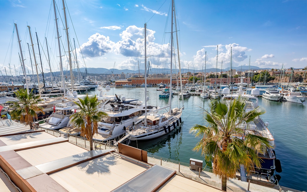 Boats docked at Palma Port in Mallorca with cityscape and mountains in the background.