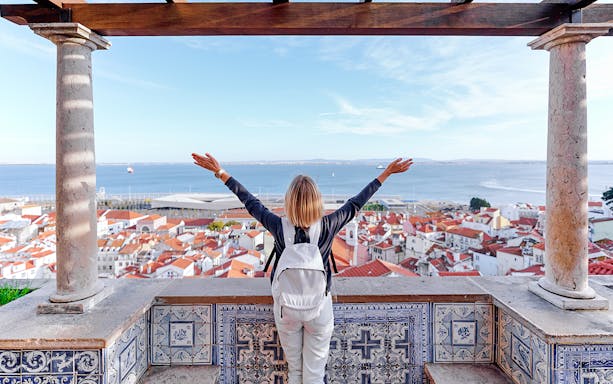 Person enjoying view from Santa Luzia Viewpoint over Lisbon rooftops and Tagus River.