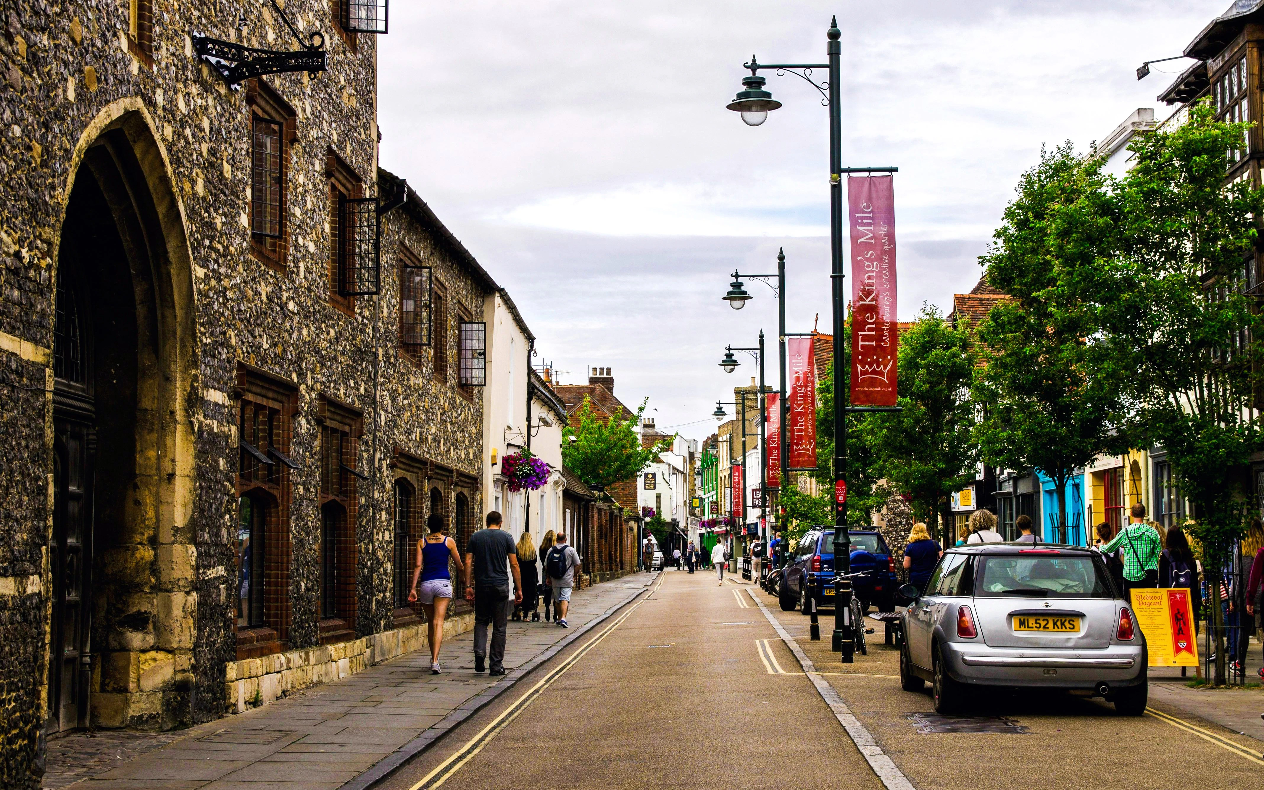 Historic street view in Canterbury, UK, with stone buildings and pedestrians.