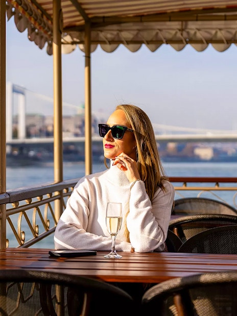 Woman enjoying a drink on a Budapest river cruise with bridge view.