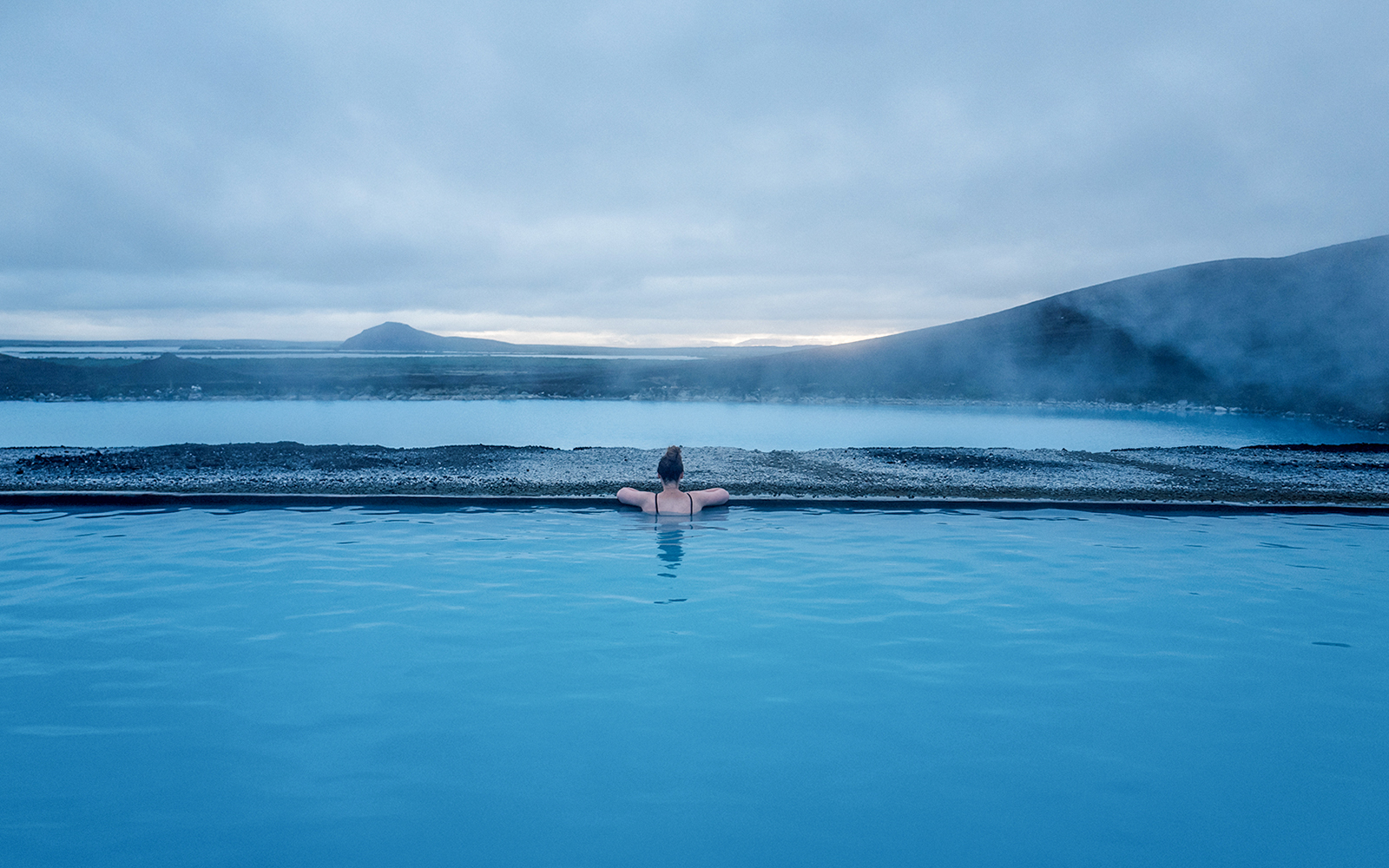 Guest relaxing in Myvatn Nature Baths with scenic Icelandic landscape.