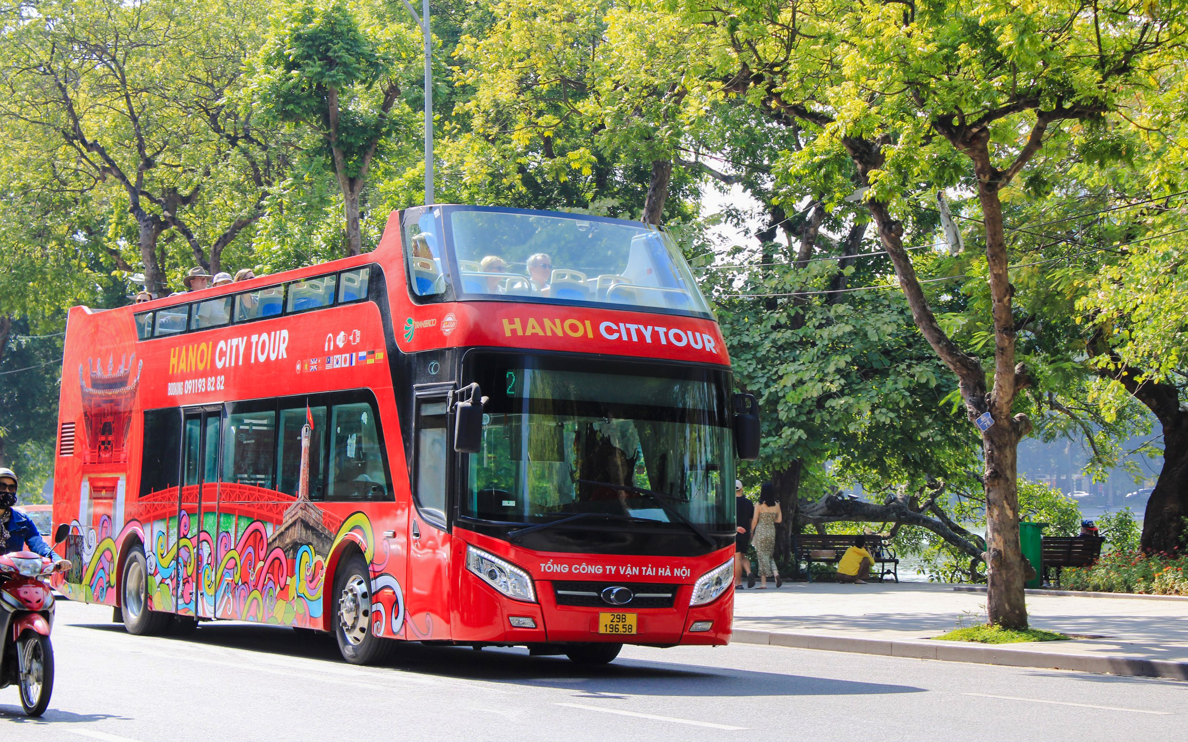 Hop on hop off tour bus driving through tree-lined street in Hanoi, Vietnam.
