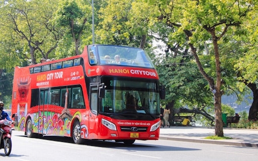 Hop on hop off tour bus driving through tree-lined street in Hanoi, Vietnam.