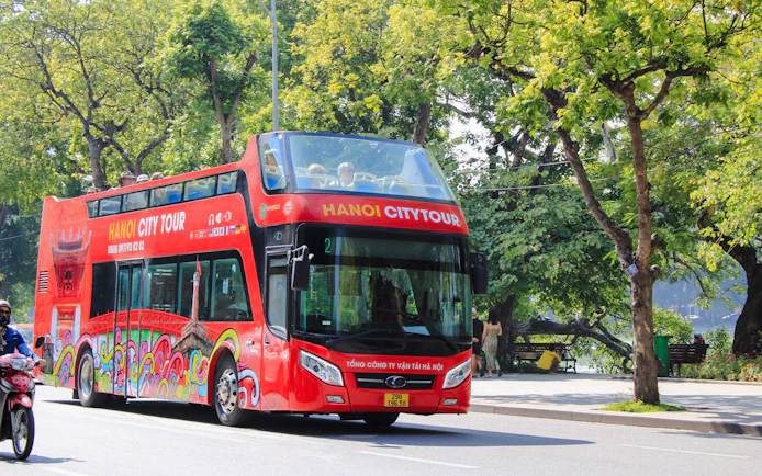 Hop on hop off tour bus driving through tree-lined street in Hanoi, Vietnam.