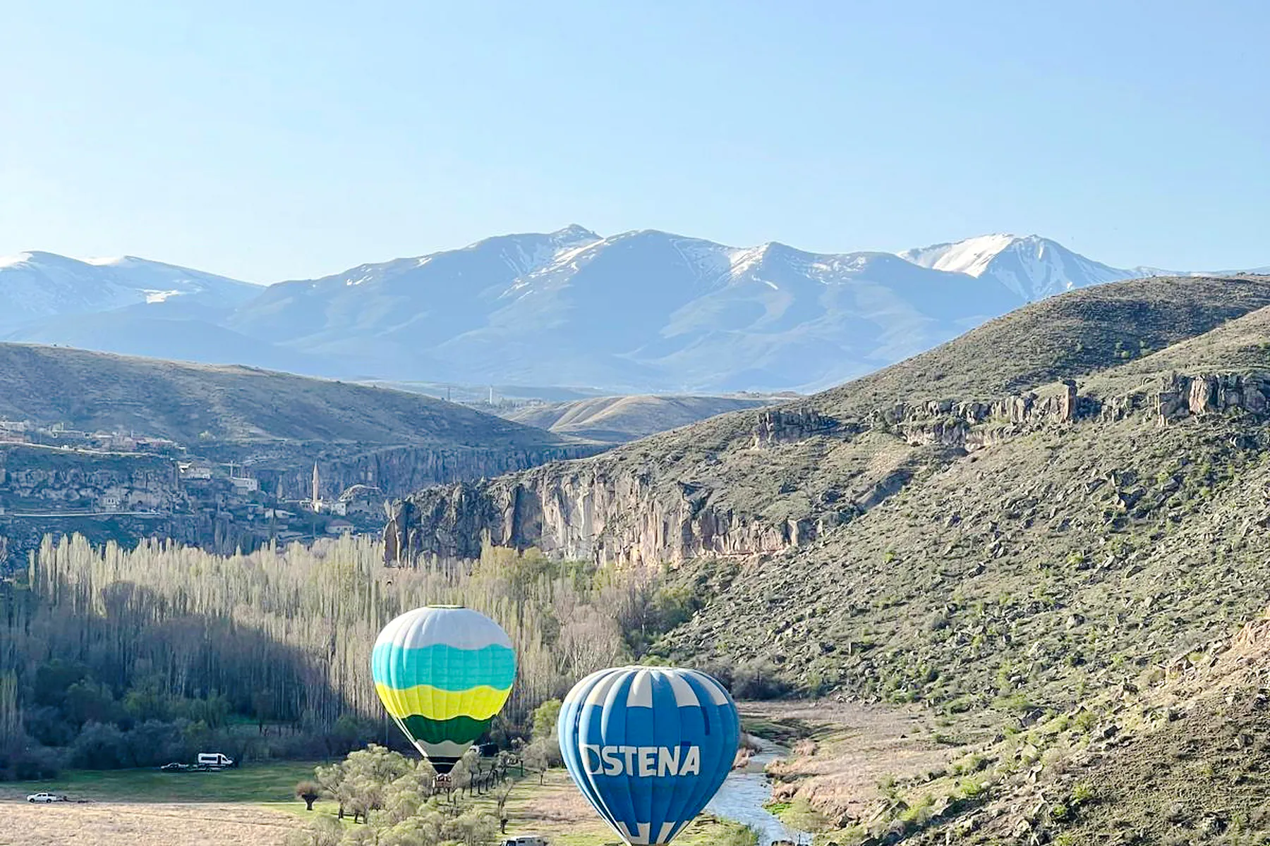 Hot air balloons over Ihlara Valley with mountains in Cappadocia.