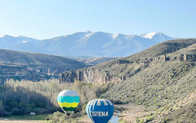 Hot air balloons over Ihlara Valley with mountains in Cappadocia.