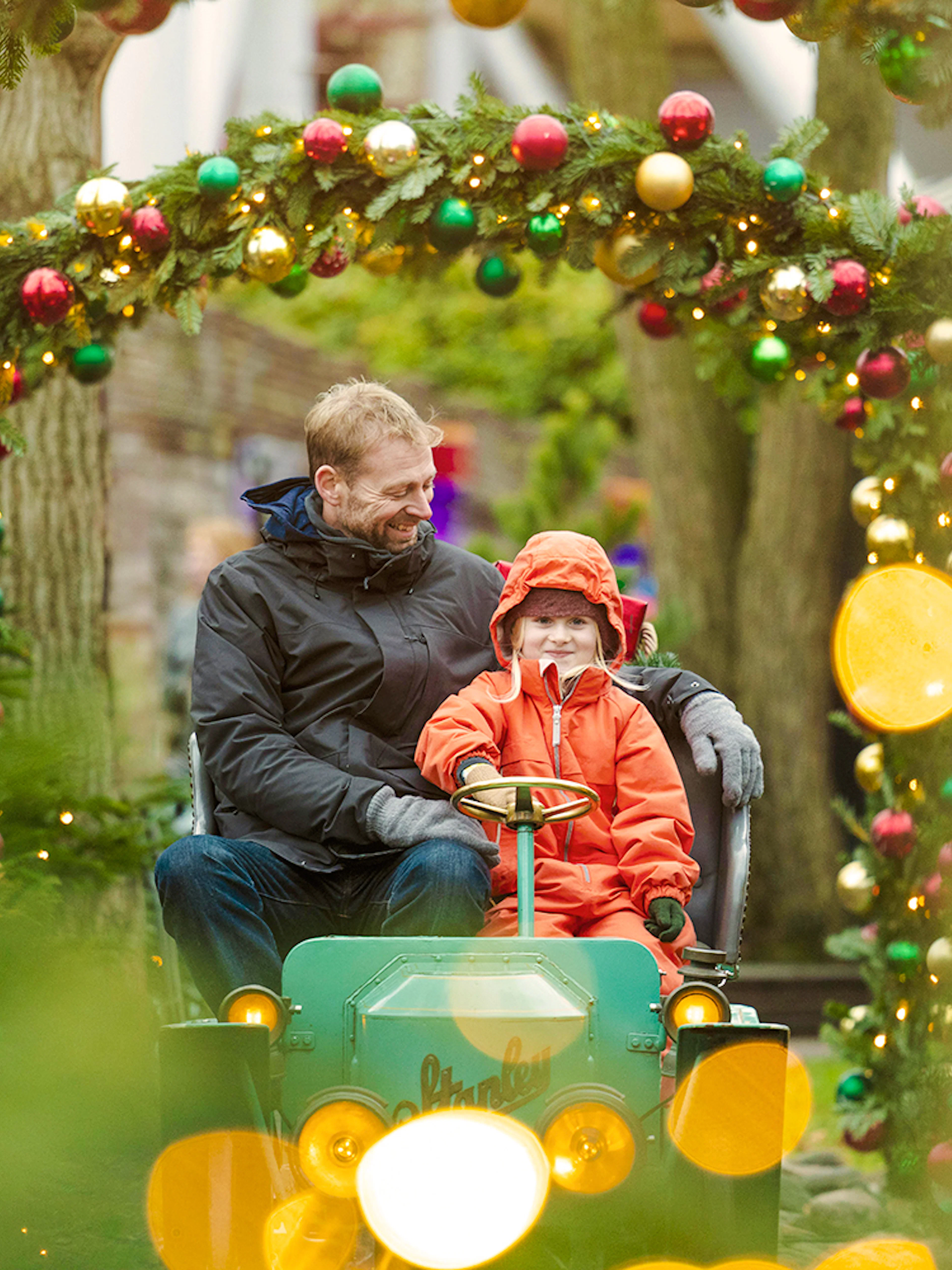 Father and child on ride at Tivoli Gardens, Copenhagen, surrounded by Christmas decorations.