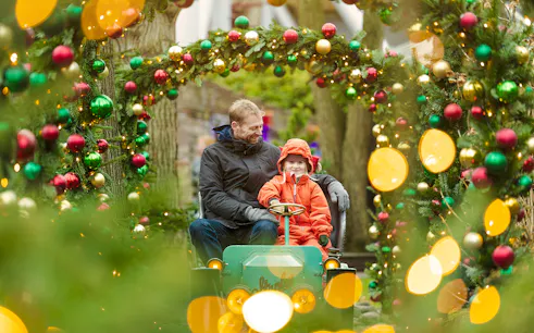 Father and child on ride at Tivoli Gardens, Copenhagen, surrounded by Christmas decorations.