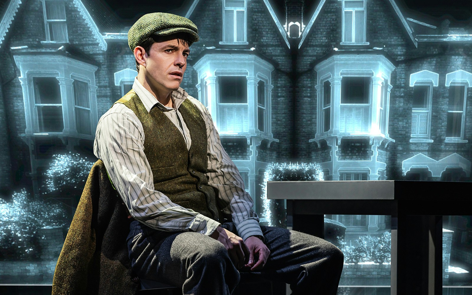 Man in period costume sitting in front of a Victorian house backdrop during The Who’s Tommy performance.