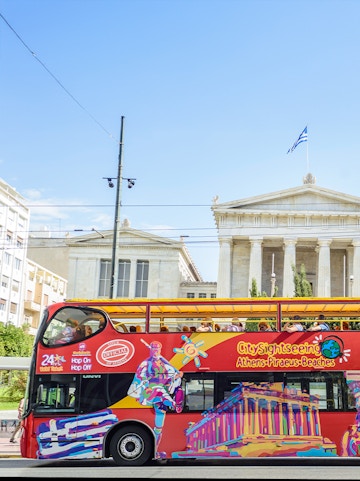 City Sightseeing Athens tour bus in front of neoclassical building with Greek flag.