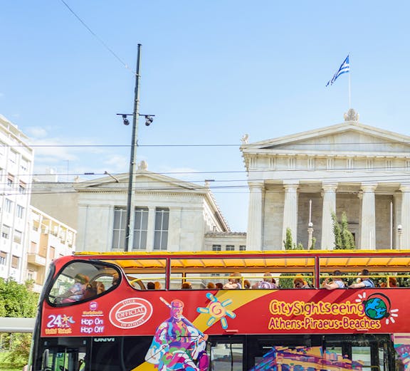 City Sightseeing Athens tour bus in front of neoclassical building with Greek flag.