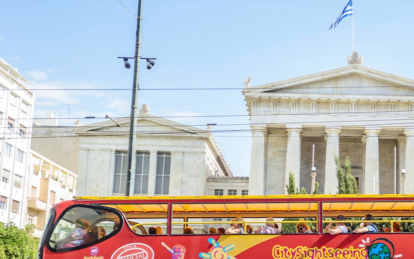 City Sightseeing Athens tour bus in front of neoclassical building with Greek flag.
