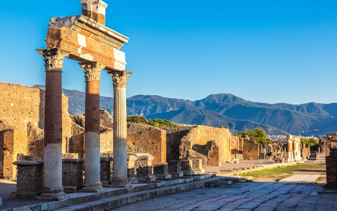 Ancient columns and ruins at Pompeii with mountains in the background.