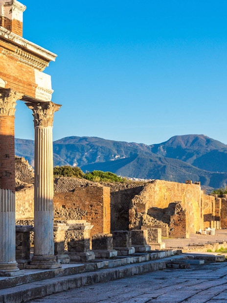 Ancient columns and ruins at Pompeii with mountains in the background.