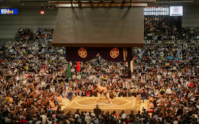 Sumo wrestlers competing in Fukuoka arena during Grand Sumo Tournament with audience.