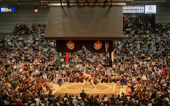 Sumo wrestlers competing in Fukuoka arena during Grand Sumo Tournament with audience.