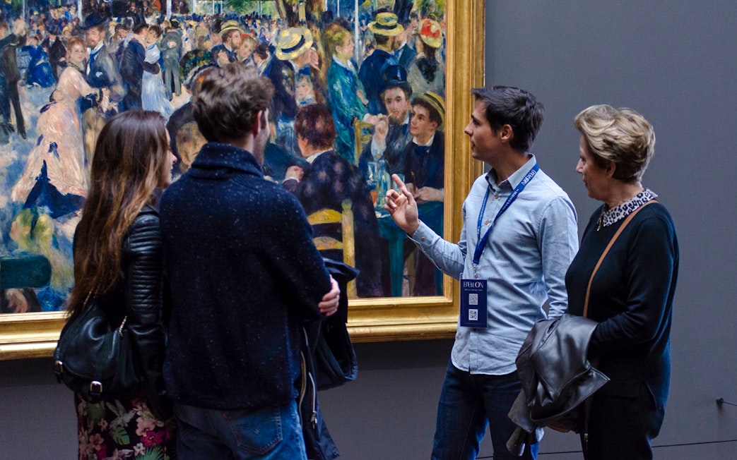 Guide explaining painting to tourists inside Orsay Museum, France.