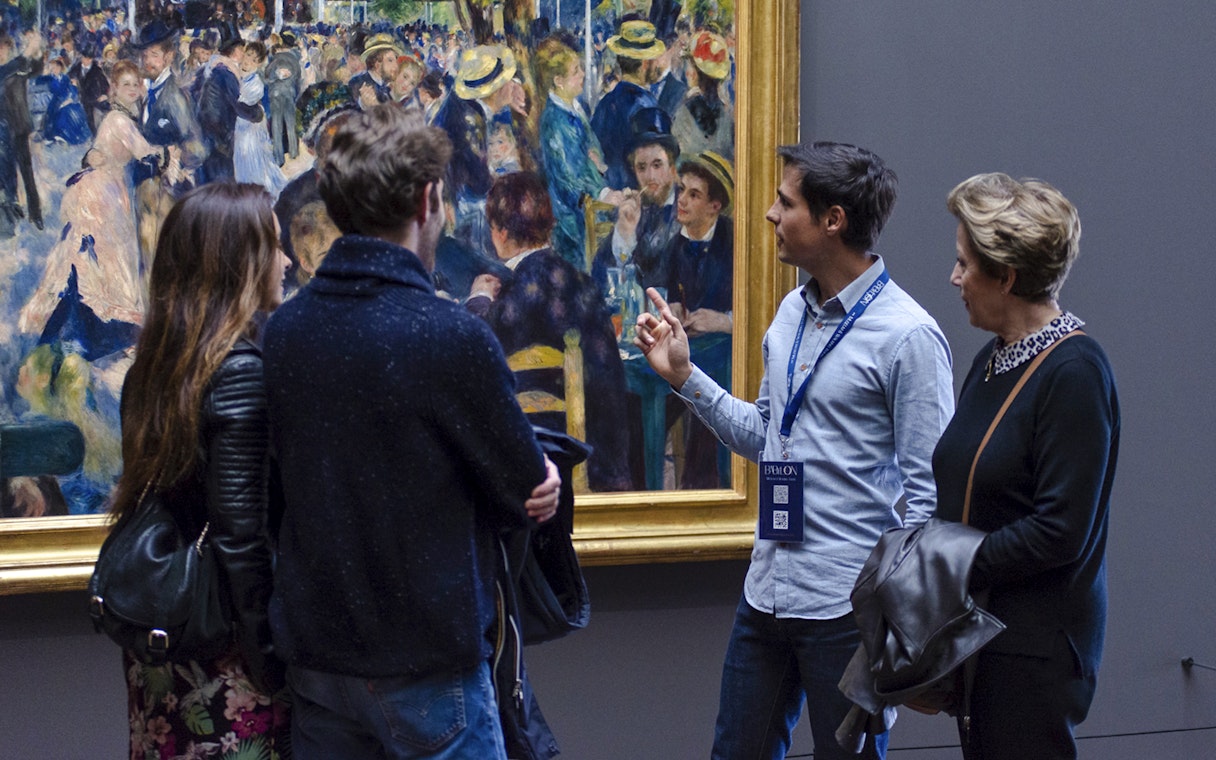 Guide explaining painting to tourists inside Orsay Museum, France.