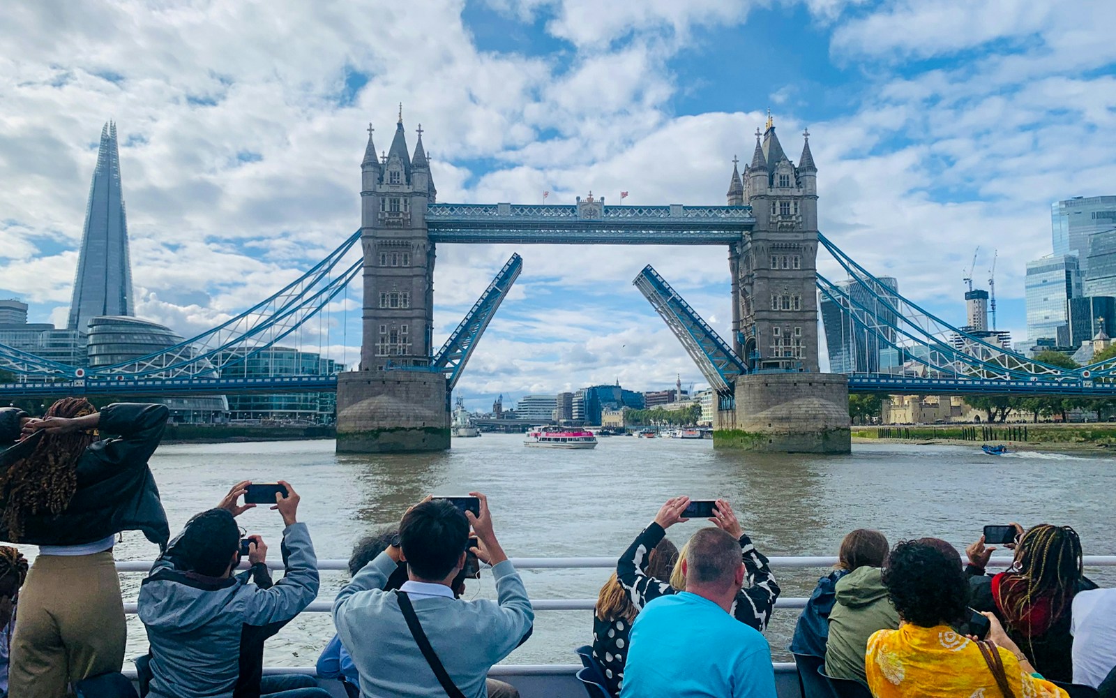 Tourists photographing Tower Bridge opening during a sightseeing cruise on the River Thames, London.