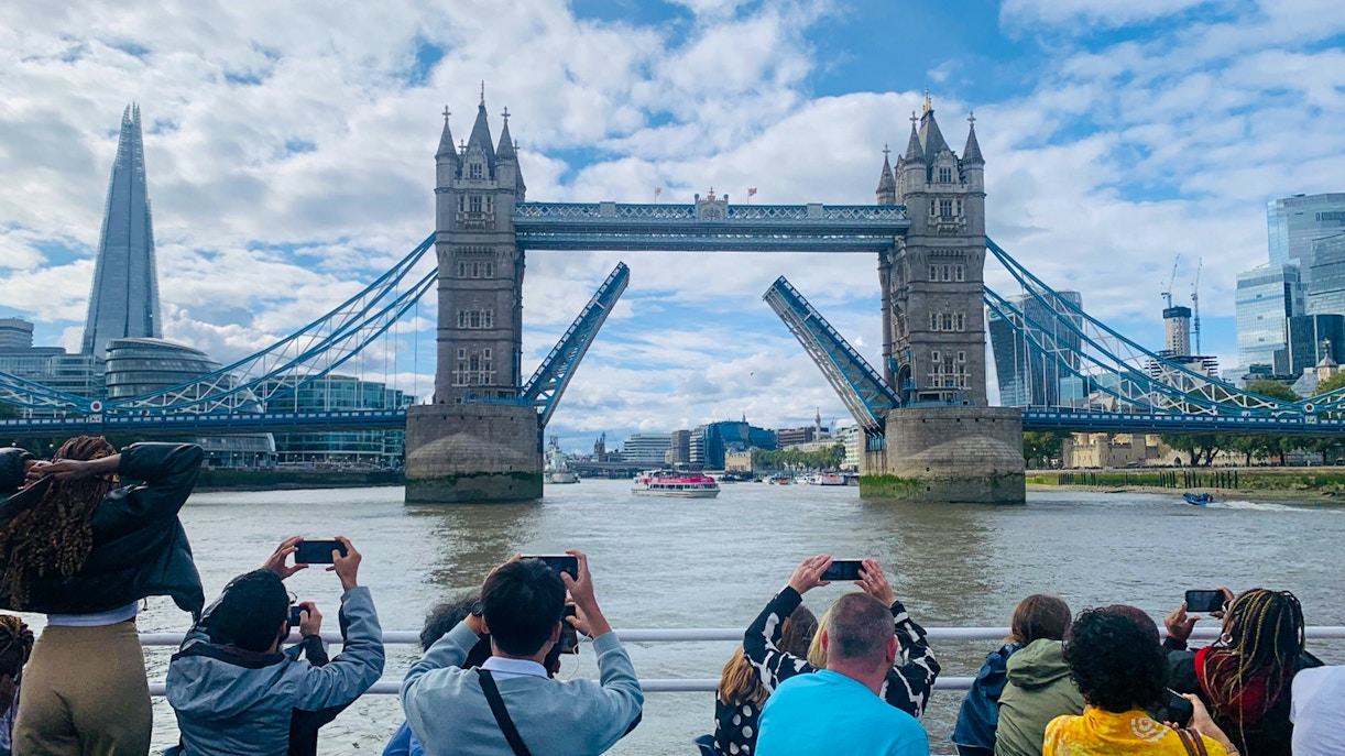 Tourists photographing Tower Bridge opening during a sightseeing cruise on the River Thames, London.