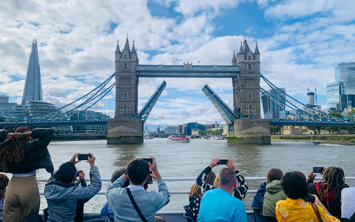 Tourists photographing Tower Bridge opening during a sightseeing cruise on the River Thames, London.