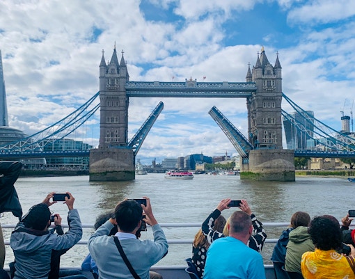 Tourists photographing Tower Bridge opening during a sightseeing cruise on the River Thames, London.