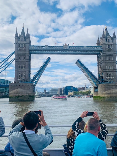 Tourists photographing Tower Bridge opening during a sightseeing cruise on the River Thames, London.