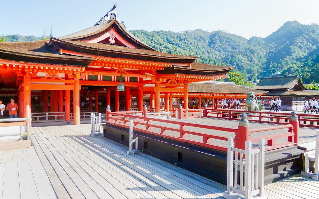 Itsukushima Shrine with red wooden structures and mountainous backdrop in Japan.