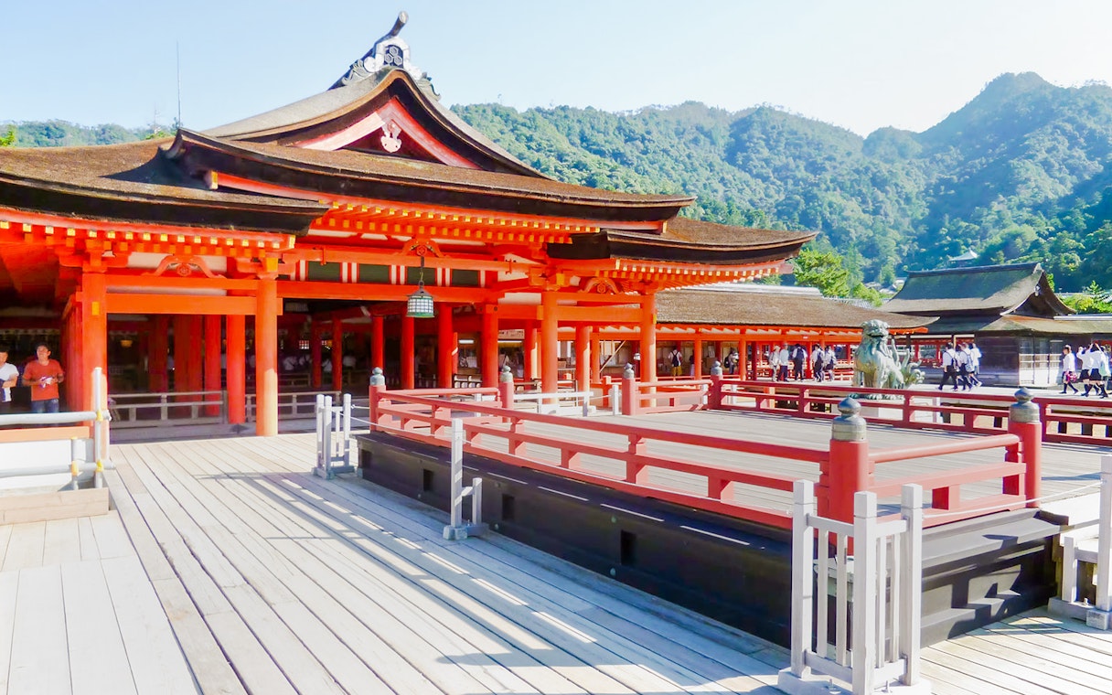 Itsukushima Shrine with red wooden structures and mountainous backdrop in Japan.